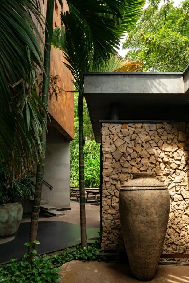 A tall clay urn stands before a wall of stacked split stone under palms.