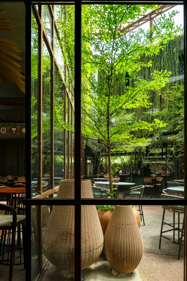 Woven vases stand by a glass wall looking out on the green courtyard.