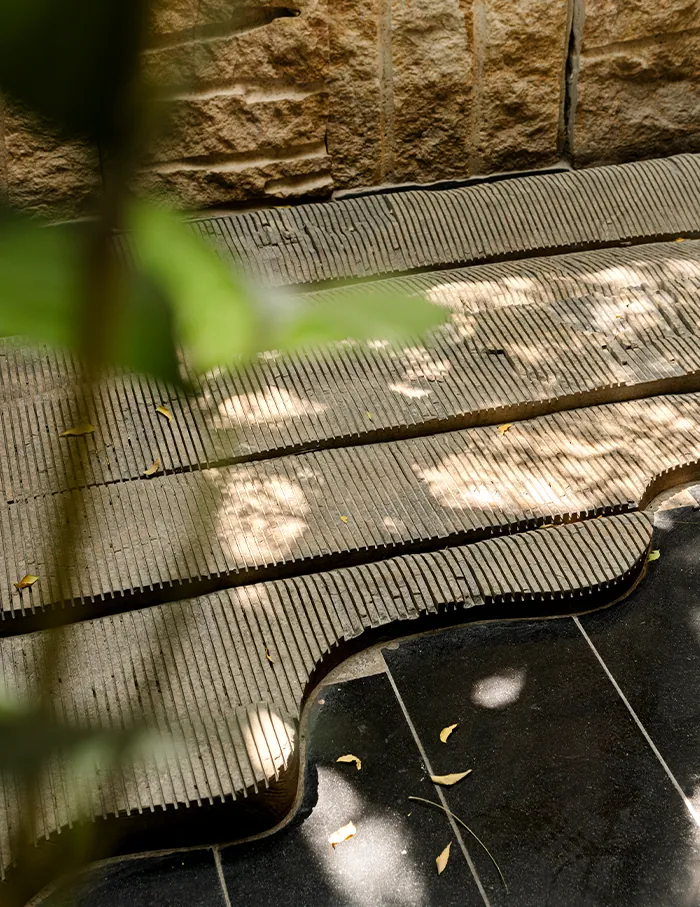 Close up: dappled light falls across timber decking and polished black stone set with small bright flecks.