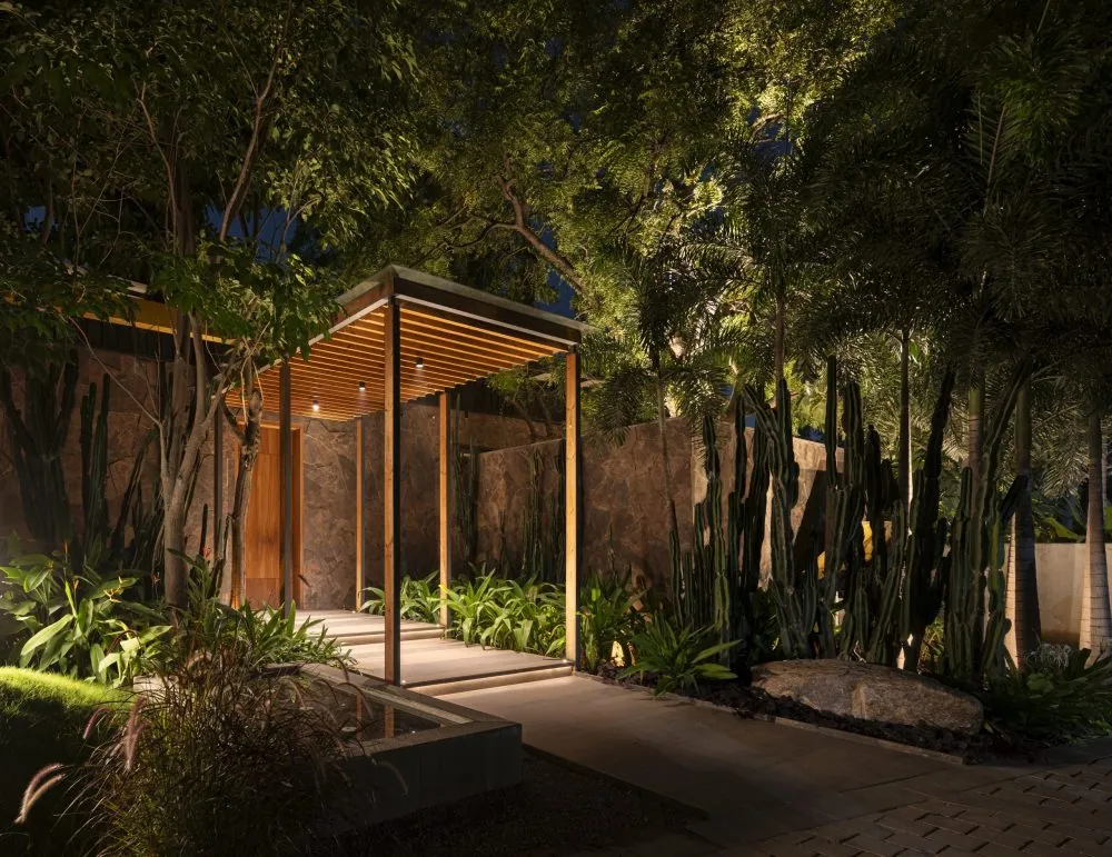 A lit timber pergola at night, surrounded by dark planting.