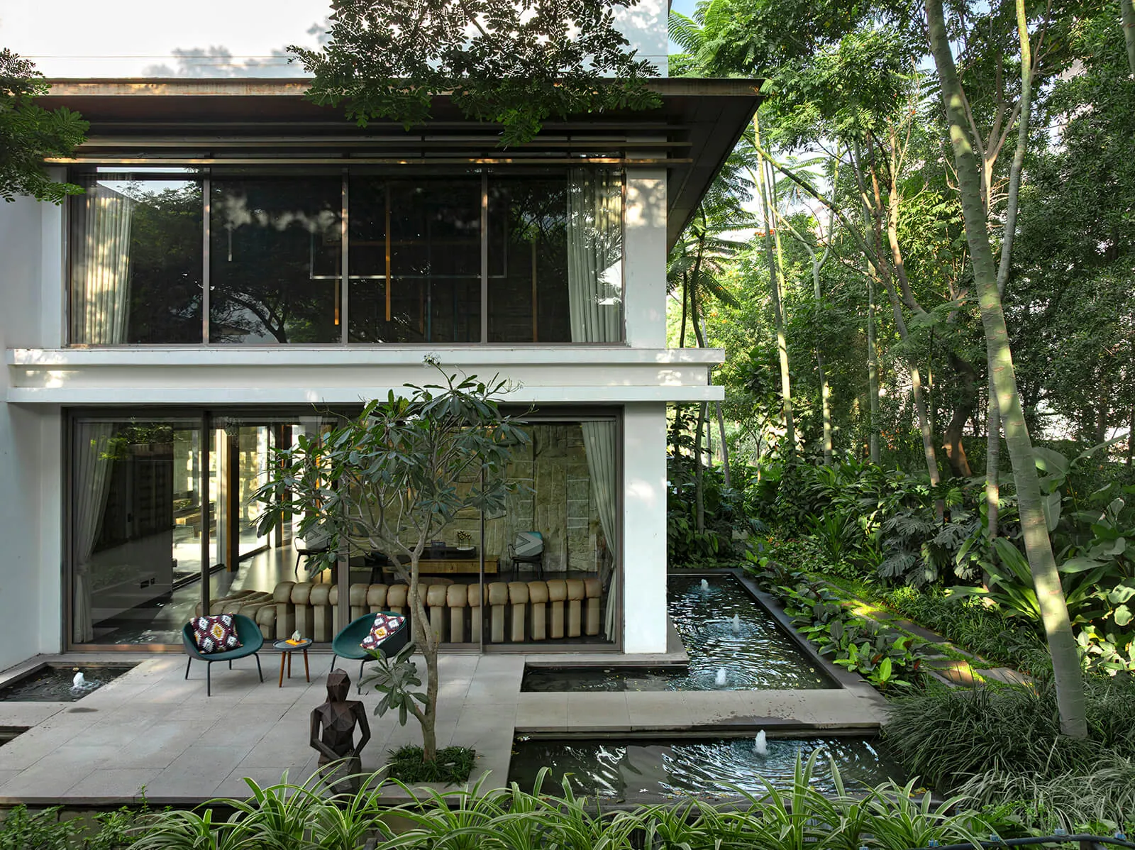 A two-storey house opens onto a courtyard with a long pool, planting and a small sculpture.