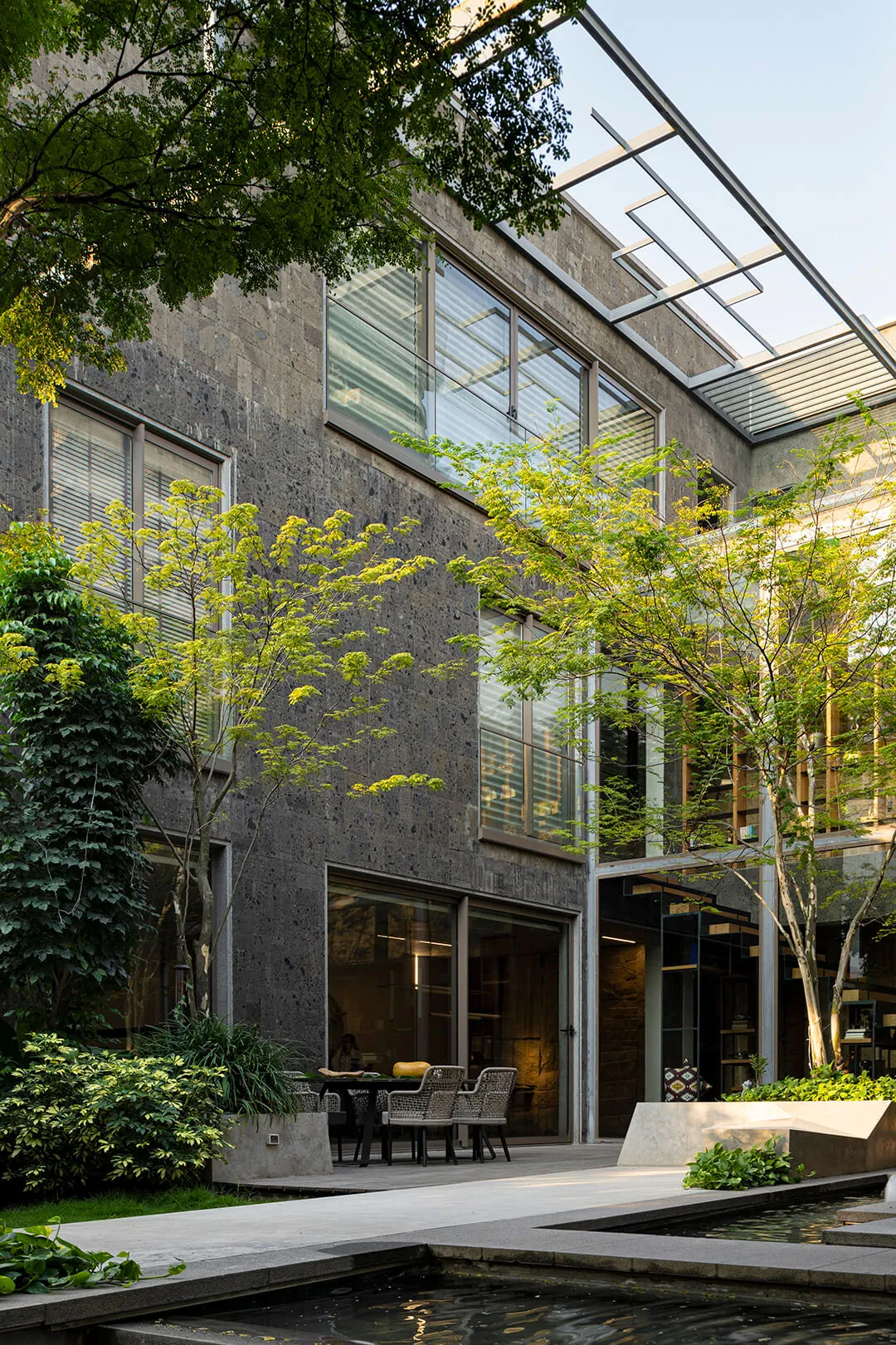 A slender tree rises in the courtyard between the house's dark stone walls and glass.