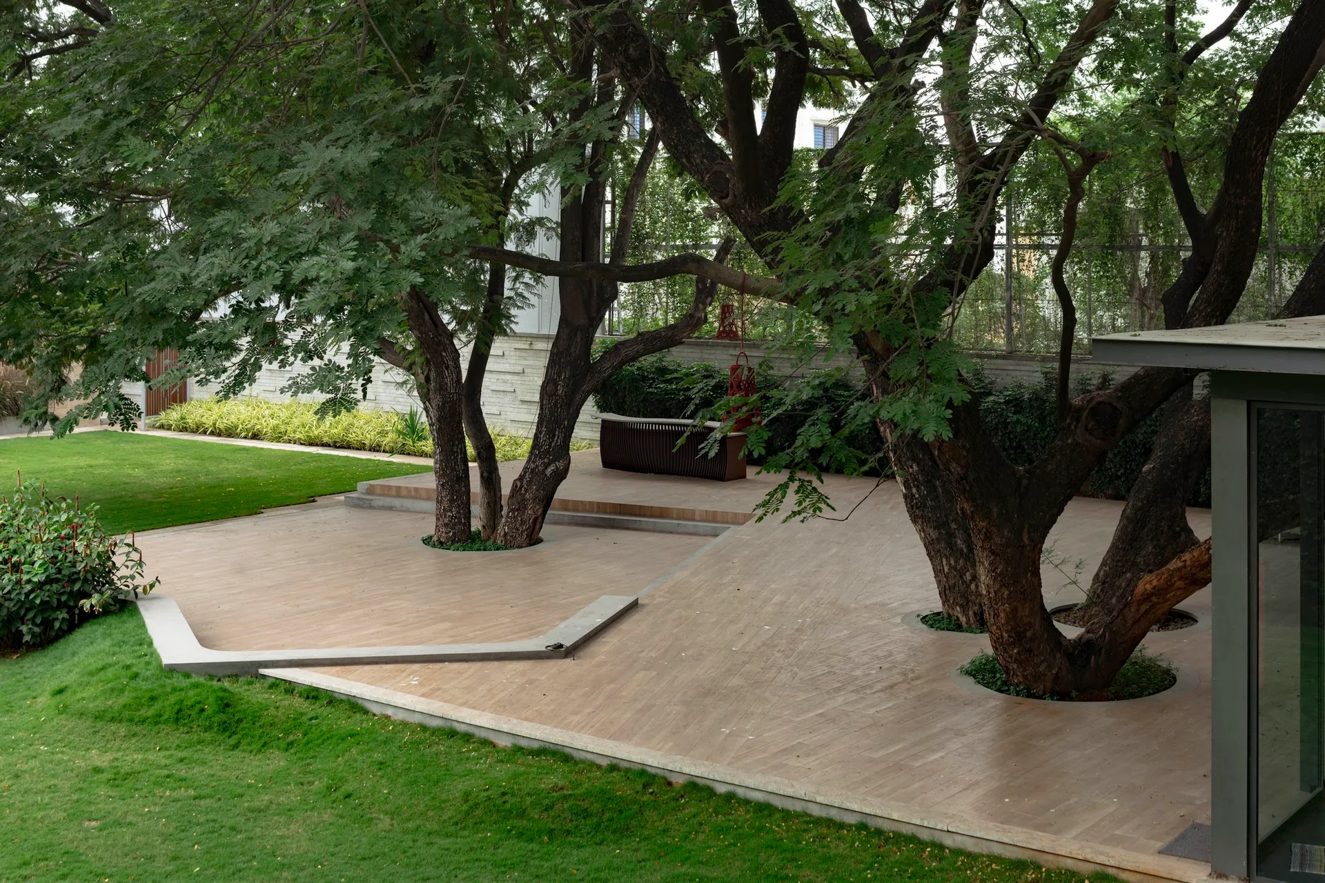 Mature trees grow through an angular stone deck at the edge of a lawn.