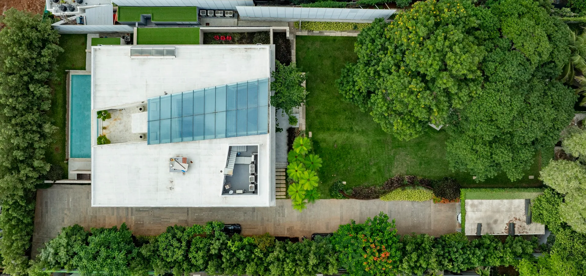 Aerial view of the house, pool and lawn, with a dense tree canopy on the right.