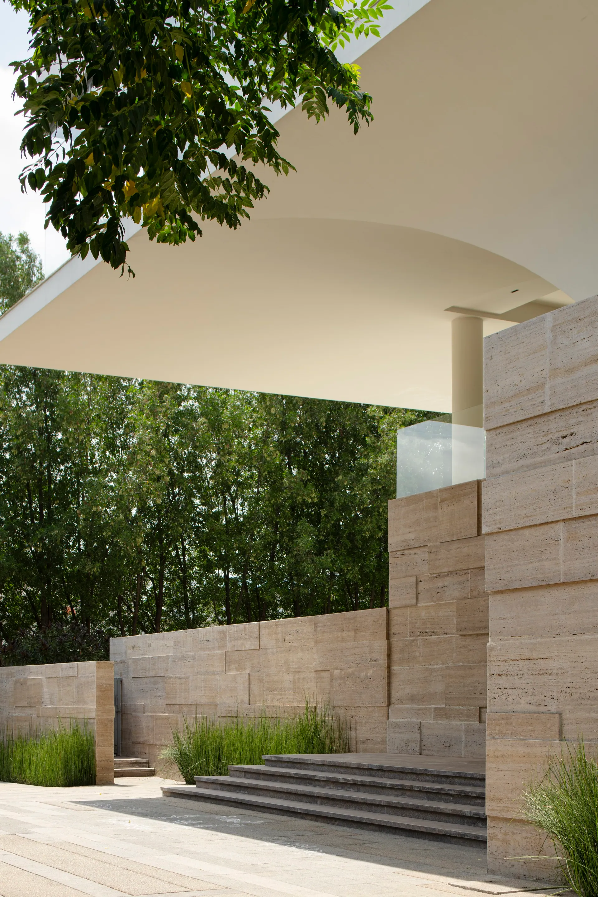 Under the white overhang of the house, stone steps lead down past a travertine wall into the garden.